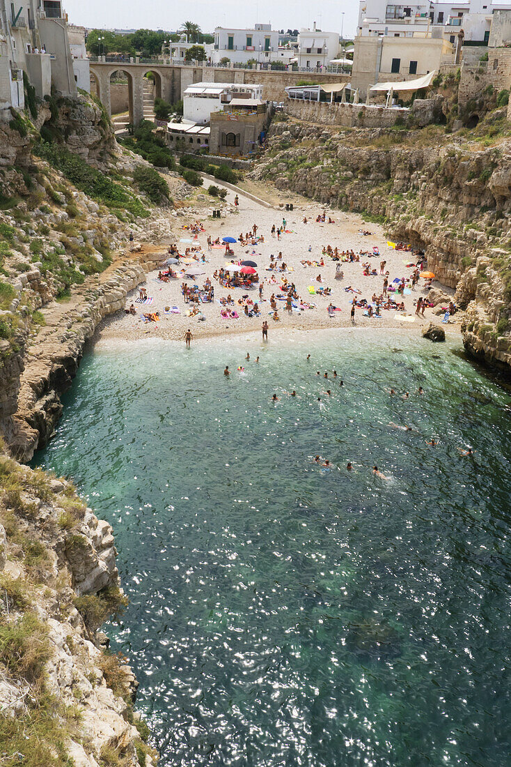 Polignano a Mare beach has golden sand that slips into bright clear green water, lined by sheer cliffs, Polignare del Mare, Puglia, Italy