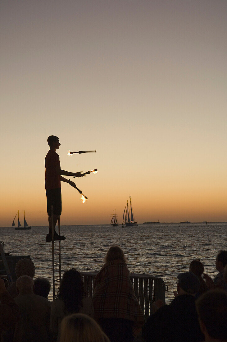 Juggler using lighted torches entertains crowd who have come to watch sunset at Mallory Square, Key West, Florida Keys, USA
