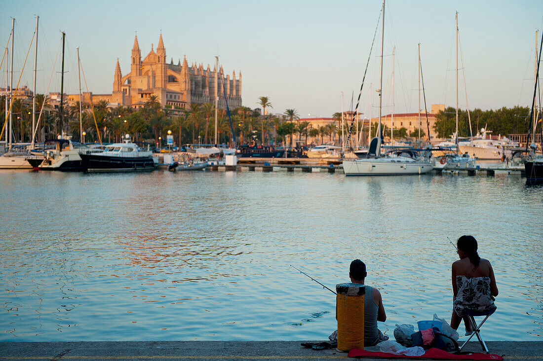 Couple fishing in harbor in front of cathedral at dusk, Palma, Majorca, Spain