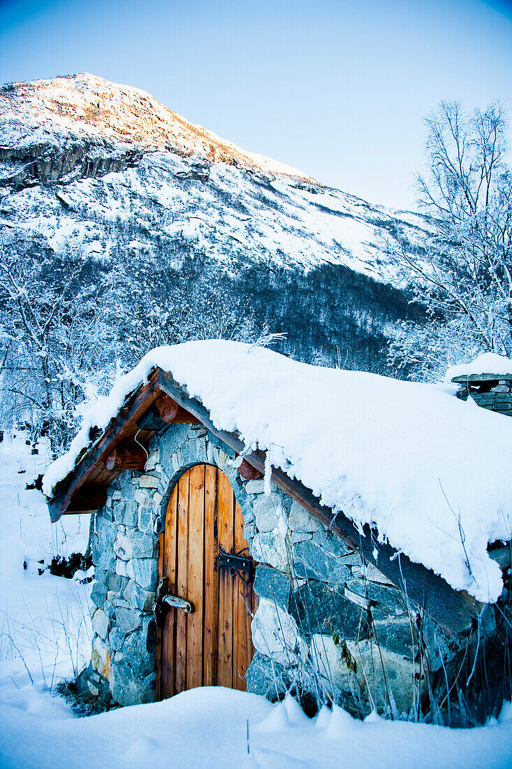 Snowy alpine scenery, snow covered traditional stone building which houses hydro electric generator, Ortnevik, Sognefjord, Norway