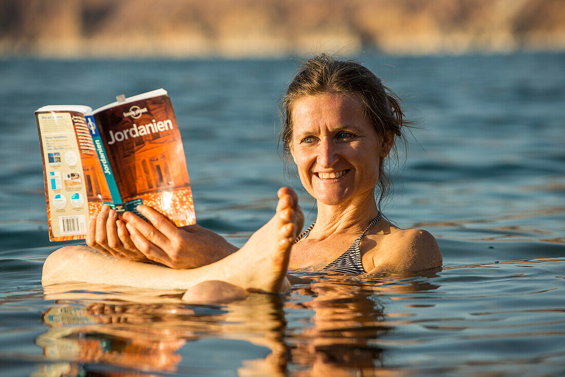 Frau liest einen Reiseführer im Toten Meer, Jordanien, Naher Osten