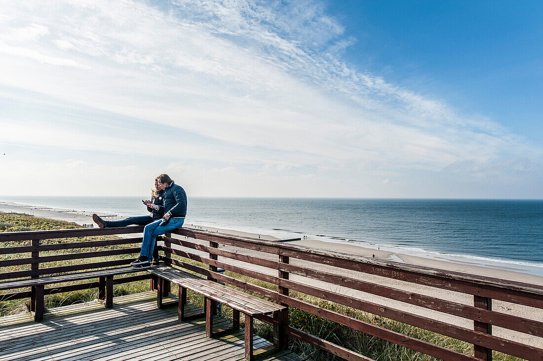 Two people sitting on a balustrade at beach, Wenningstedt-Braderup, Sylt, Schleswig-Holstein, Germany