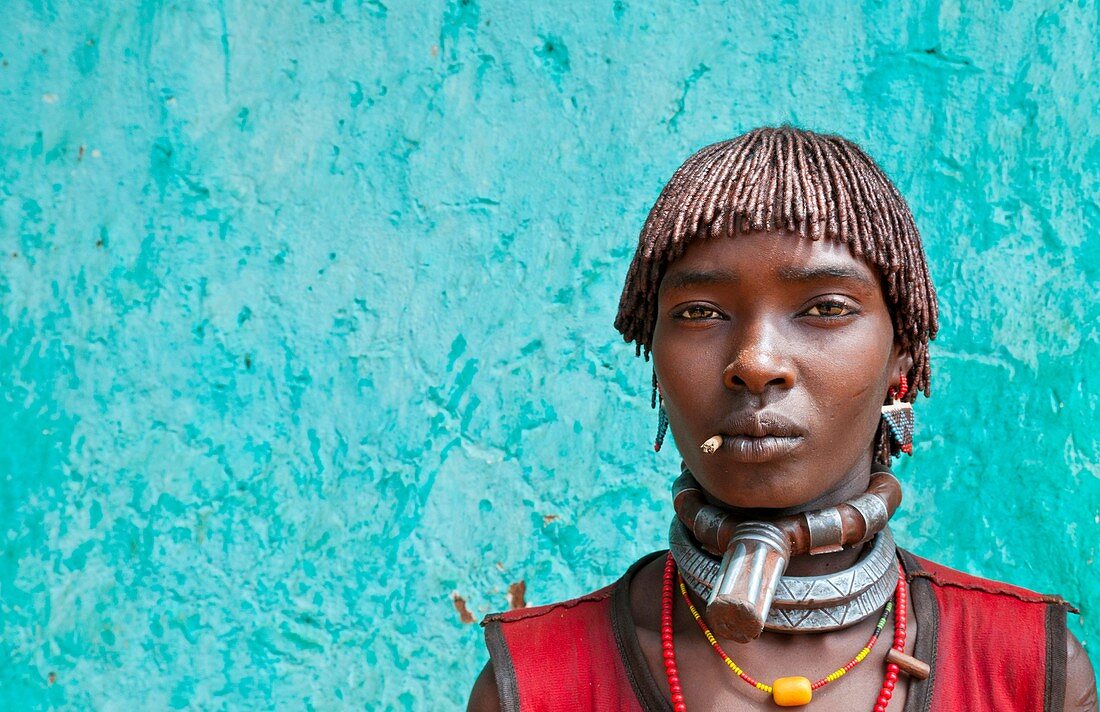 Dimeka Ethiopia Africa village Lower Omo Valley portrait of attractive Hamar woman with necklace showing First Wife against green wall 19