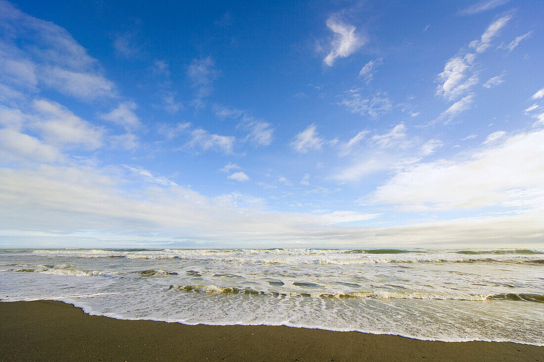 High tide surf spreading foam on golden beach in Kahurangi National Park, Pacific Ocean in evening, winter, Westland, South Island, New Zealand