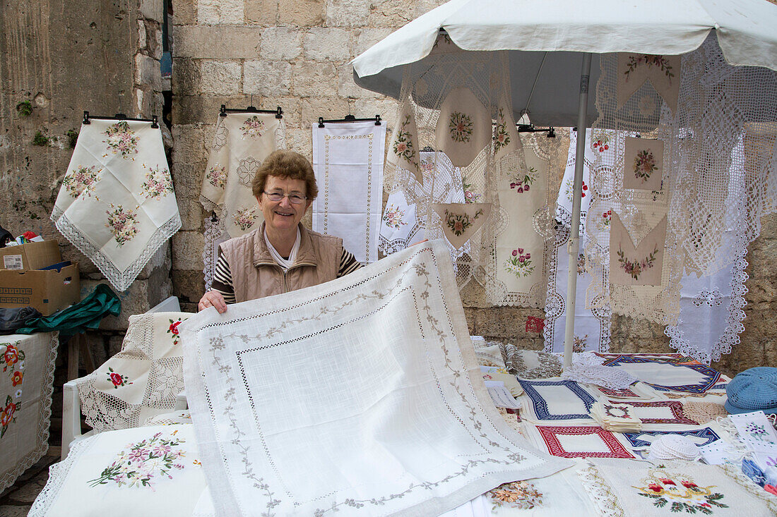Frau zeigt Tischdecke mit Stickerei an einem Marktstand in der Altstadt, Dubrovnik, Dalmatien, Kroatien, Europa