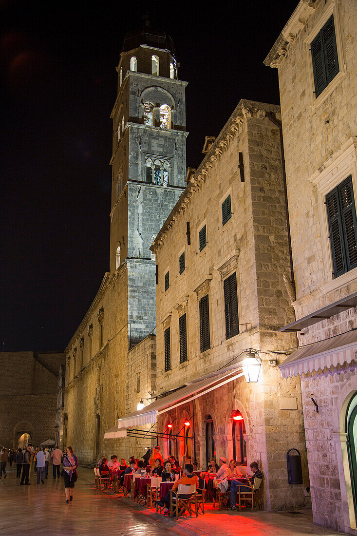 Menschen sitzen draußen vor einem Restaurant an der Stradun Hauptgasse der Altstadt mit Kirchturm von Franziskanerkloster am Abend, Dubrovnik, Dalmatien, Kroatien, Europa