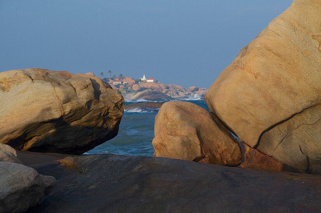 View to temples on a rocky hill on the coast, rocks on the beach at Kirinda near Gala National park, South Sri Lanka