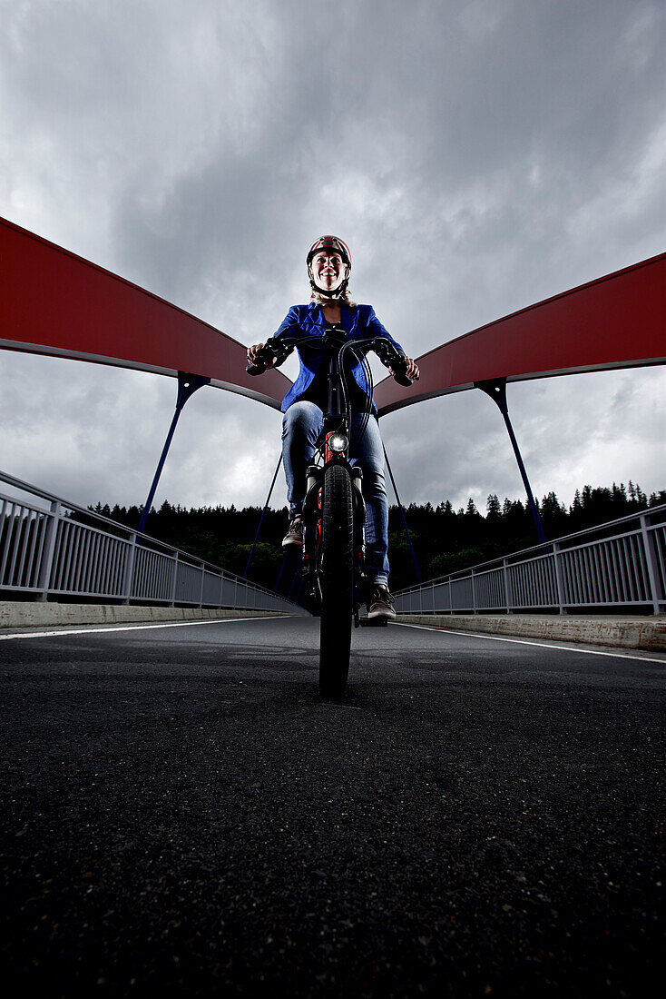 Woman riding an electric bicycle passing a bridge, Tanna, Thuringia, Germany