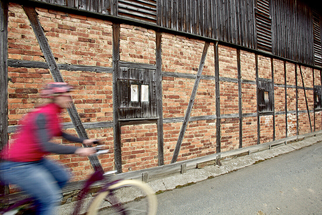 Woman riding an electric bicycle passing a half-timbered house, Tanna, Thuringia, Germany