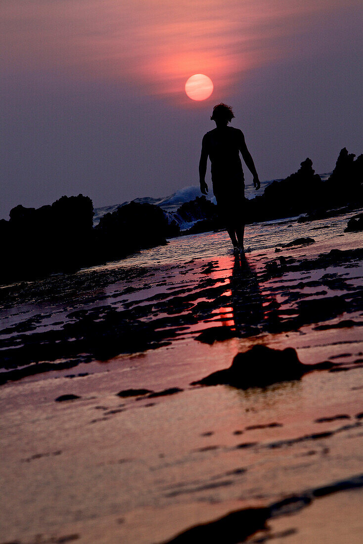 Mann geht am Strand im Sonnenuntergang entlang, Jakarta, Java, Indonesien