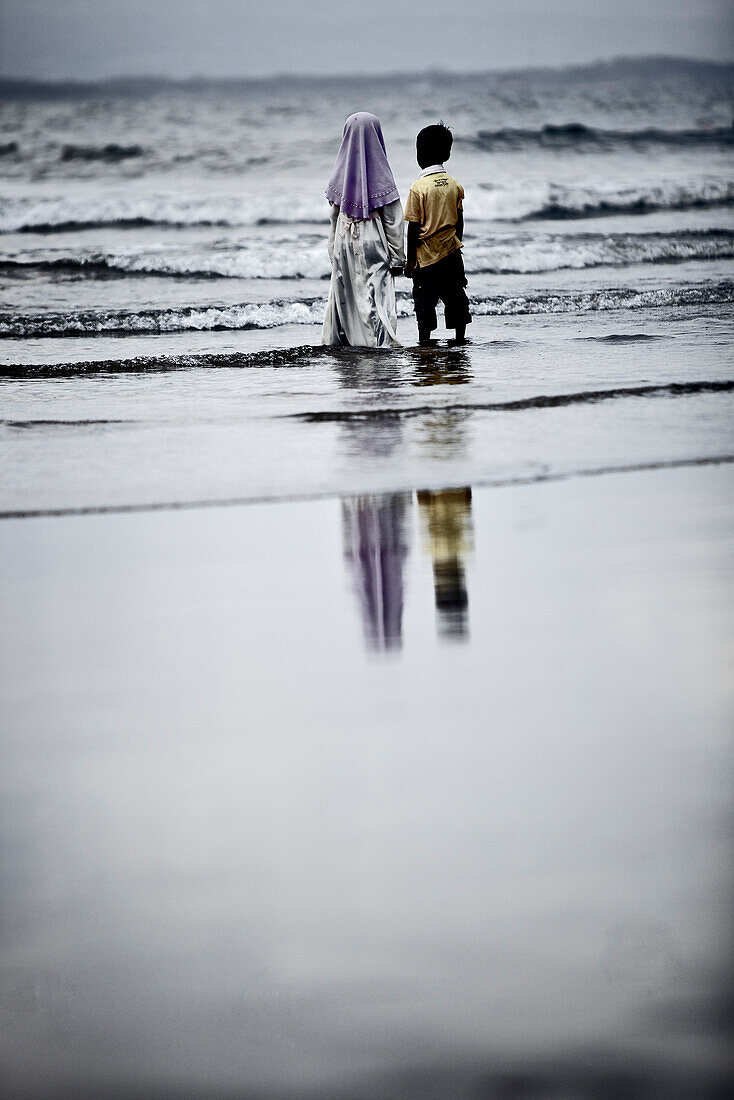 Two children standing in water at beach, Jakarta, Java, Indonesia