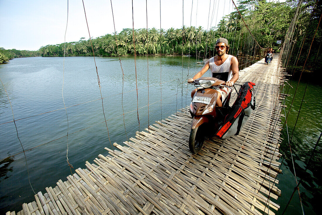 Mann fährt mit einem Motorroller über eine Hängebrücke, Jakarta, Java, Indonesien