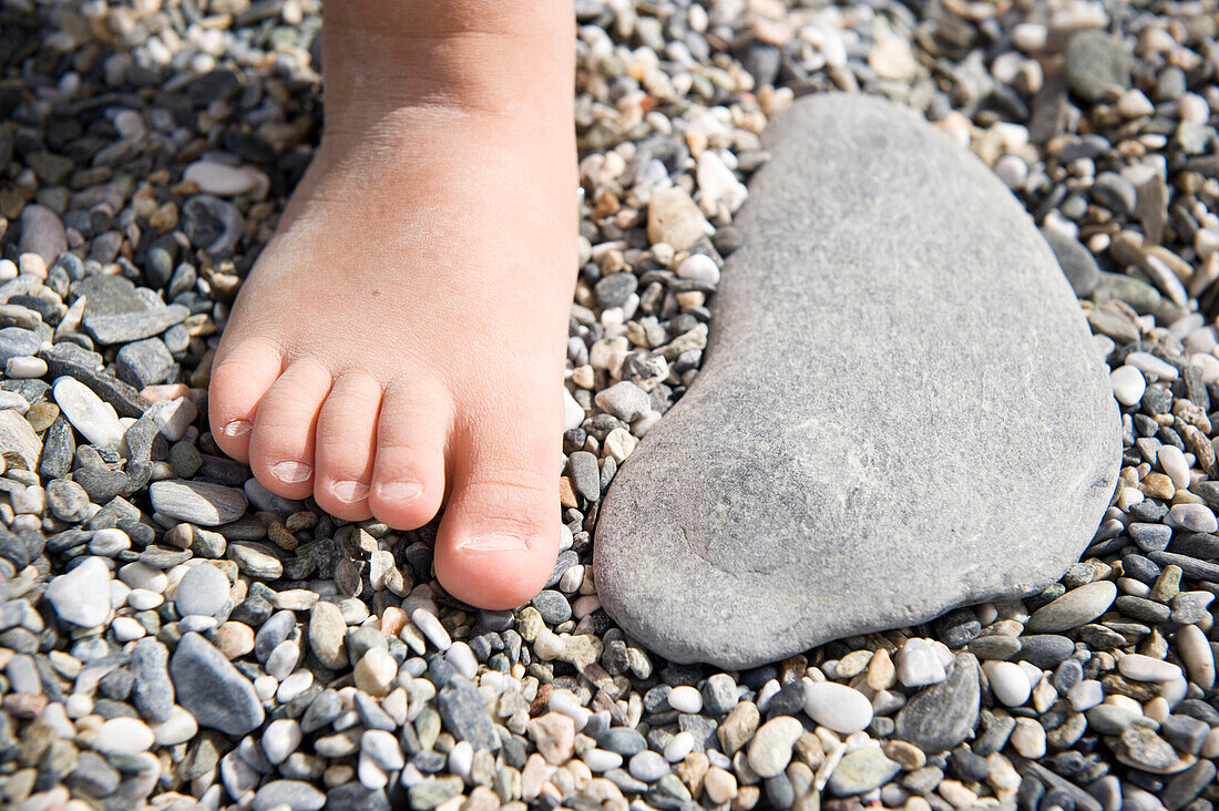 Foot of child next to a pebble at shingle beach, Andalusia, Spain