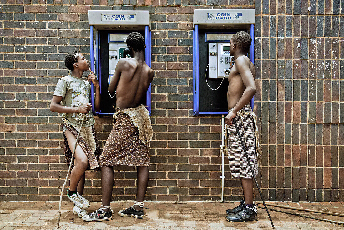 Drei junge Männer der Swazi Vilksgruppe in traditionellen Lendenstoffen telefonieren an öffentlichen Fernsprecher, Swasiland, Afrika