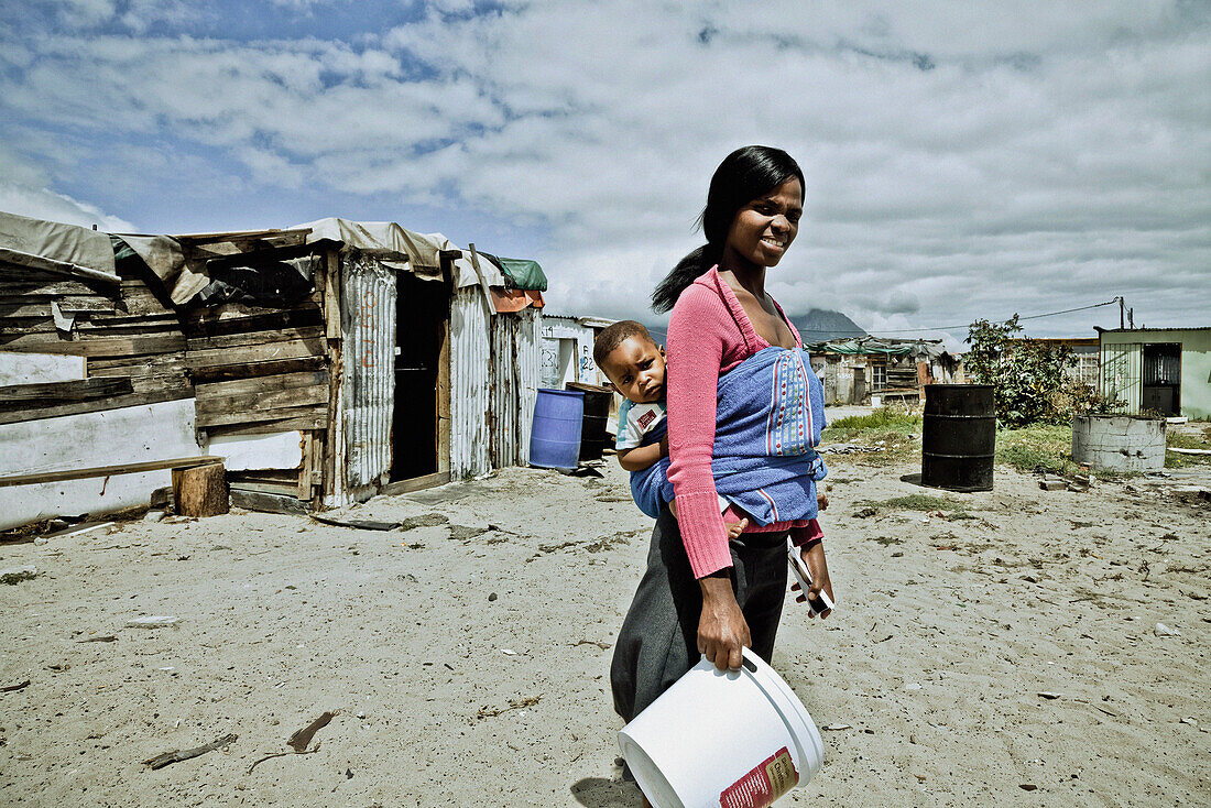 Young mother in front of shacks carrying her baby, Langa township, Cape Town, South Africa, Africa
