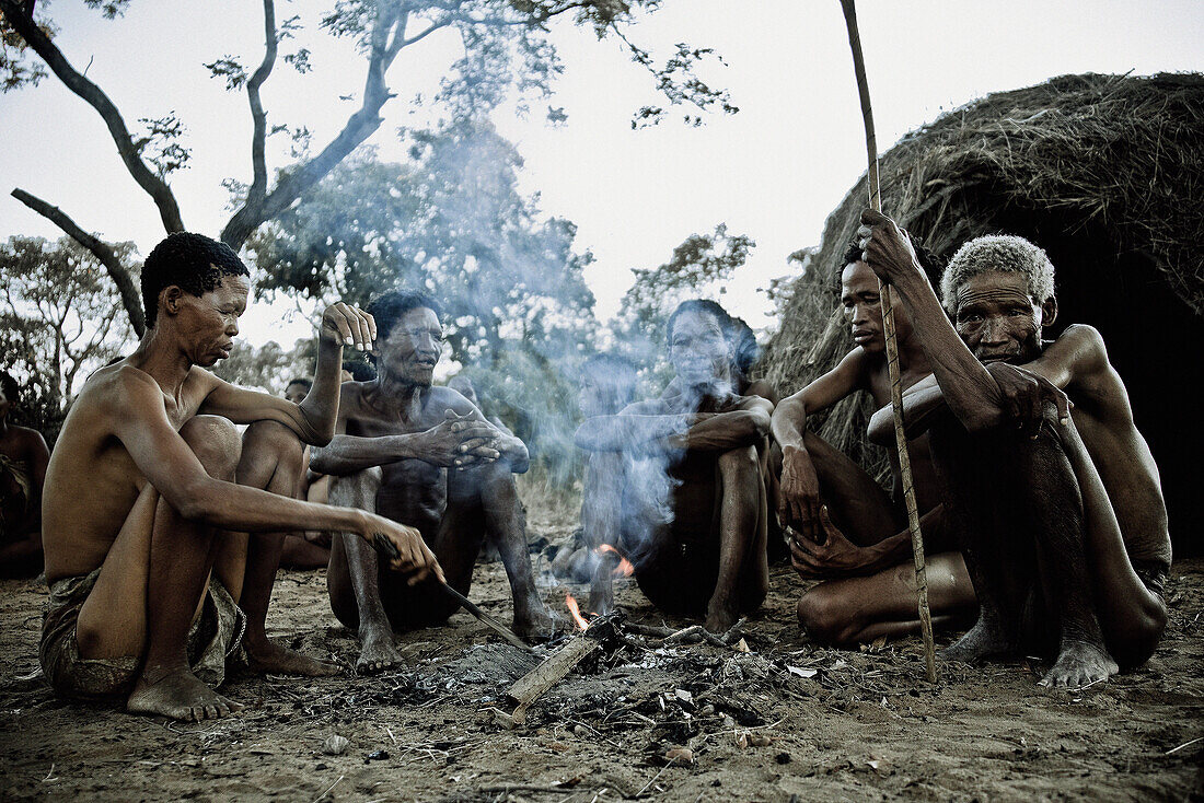 Eine Frau und vier Männer der San Volksgruppe sitzen um ein Lagerfeuer, Region Otjozondjupa, Namibia, Afrika