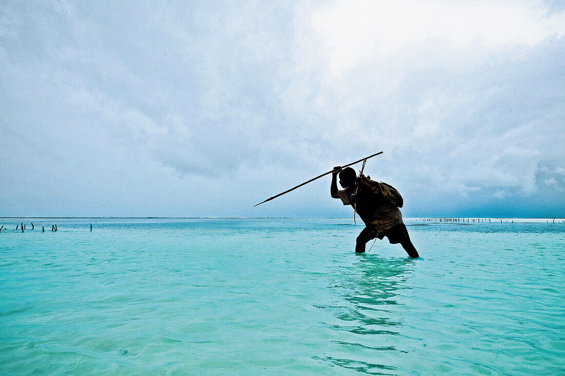 Ein Fischer mit Harpune im seichten Wasser vor der Küste Sansibars, Tansania, Afrika