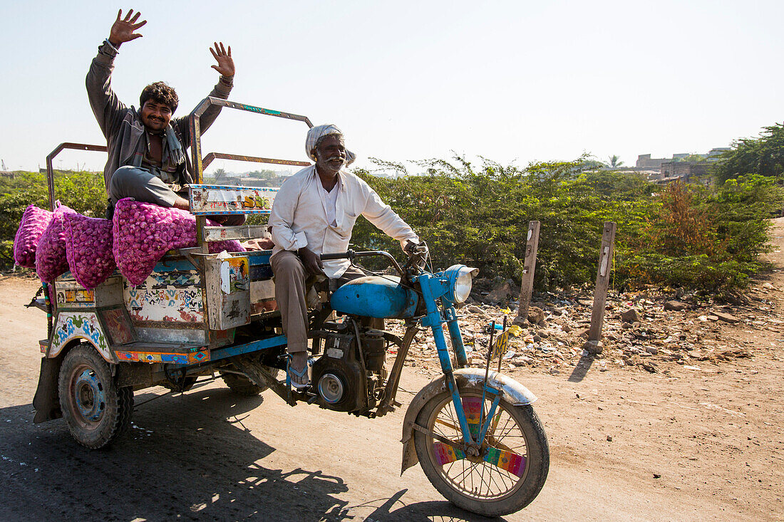 Zwei Männer mit einer Ladung Zwiebeln auf ihrer motorisierten Riksha auf dem Weg zum Markt, Porbandar, Gujarat, Indien