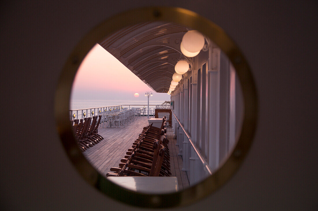 Blick durch rundes Fenster auf Deckstühle an Bord von Kreuzfahrtschiff MS Deutschland, Reederei Peter Deilmann, bei Sonnenuntergang, Arabisches Meer, nahe Indien