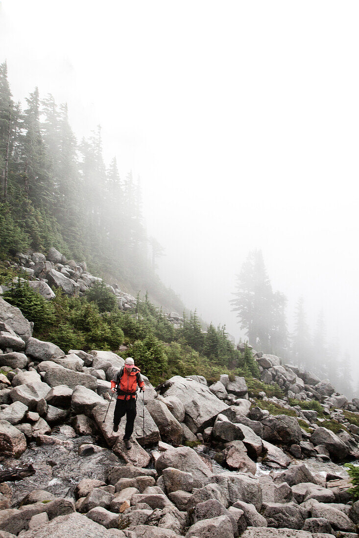 A climber crosses a stream buried beneath boulders on a foggy morning Washington, USA