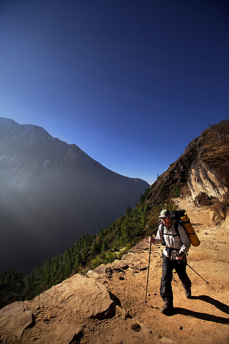 A heavily laden male trekker strides along the trail out of Namche Bazaar in Nepal Solukhumbu Region, Nepal