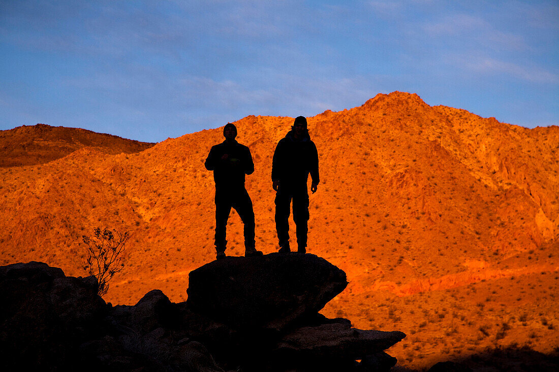 Two silhouetted male backpackers pose for a portrait while standing on a rock pile while hiking through Death Valley's Confidence Hills, California Death Valley, California, United States of America