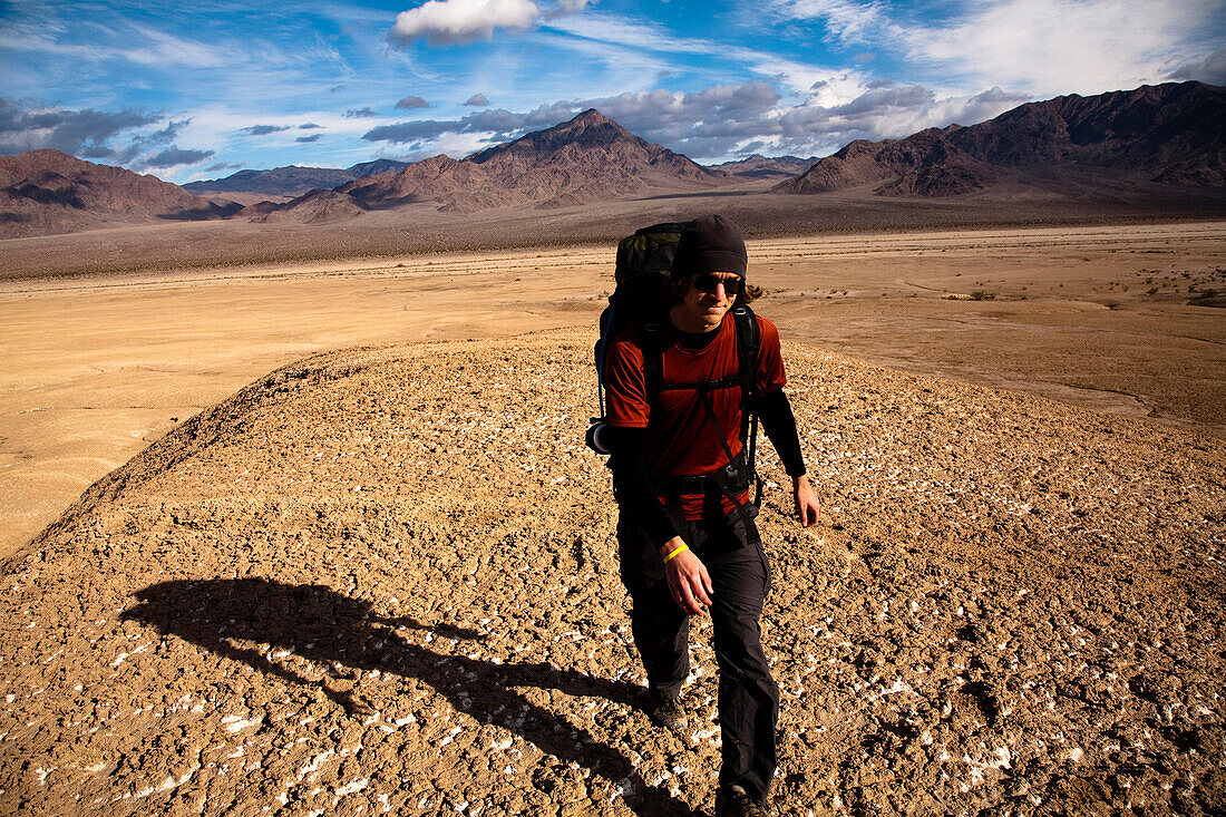 A young man backpacks through the Confidence Hills in Death Valley Nation Park, California Death Valley, California, United States of America