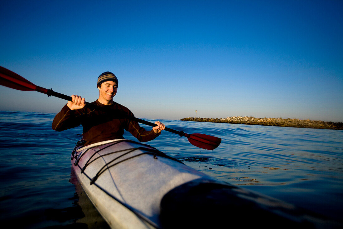 A young man smiles while paddling a touring kayak just outside of Ventura Harbor in Ventura, California Ventura, California, United States of America