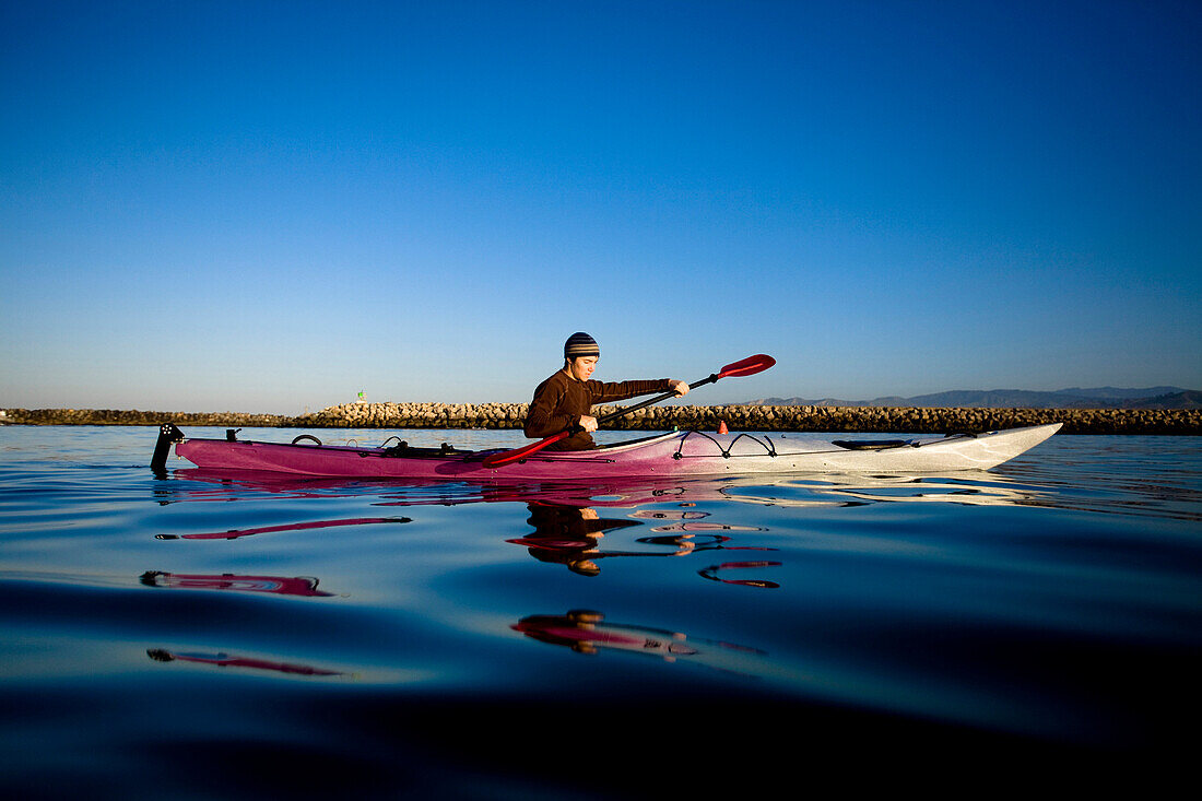 A young man looks at his reflection while paddling a touring kayak just outside of Ventura Harbor in Ventura Ventura, California, United States of America