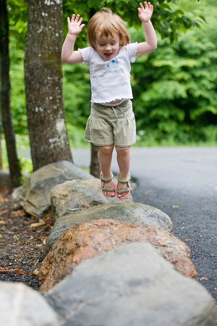 A young girl jumps between rocks Maine, USA