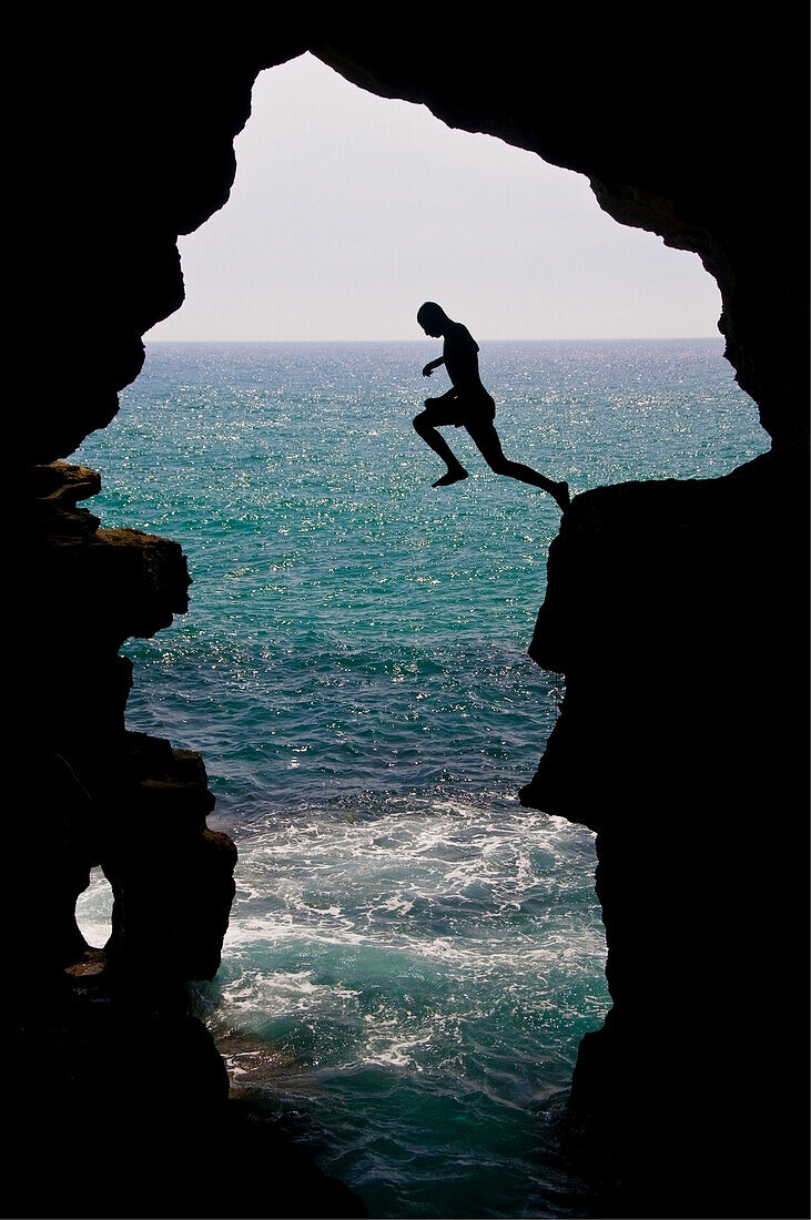 Young man silhouetted jumping into the Atlantic Ocean in the Hercules Cave near Tangier, Morocco, Tangier, Morocco