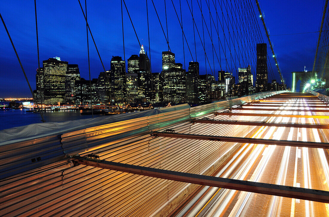 Cars pass over the Brooklyn Bridge with the New York City skyline in the background at dusk, New York New York City, New York, USA