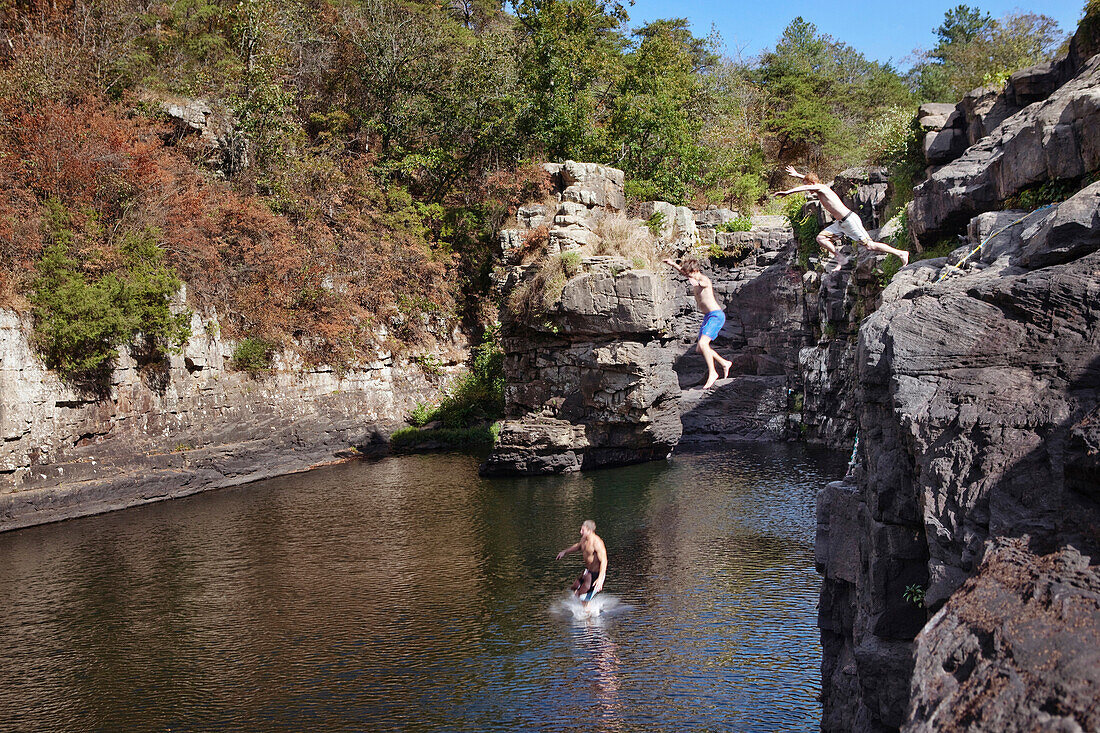 Three young men jump off rock cliffs into a lagoon at High Falls Park, Geraldine, Alabama Geraldine, Alabama, United States