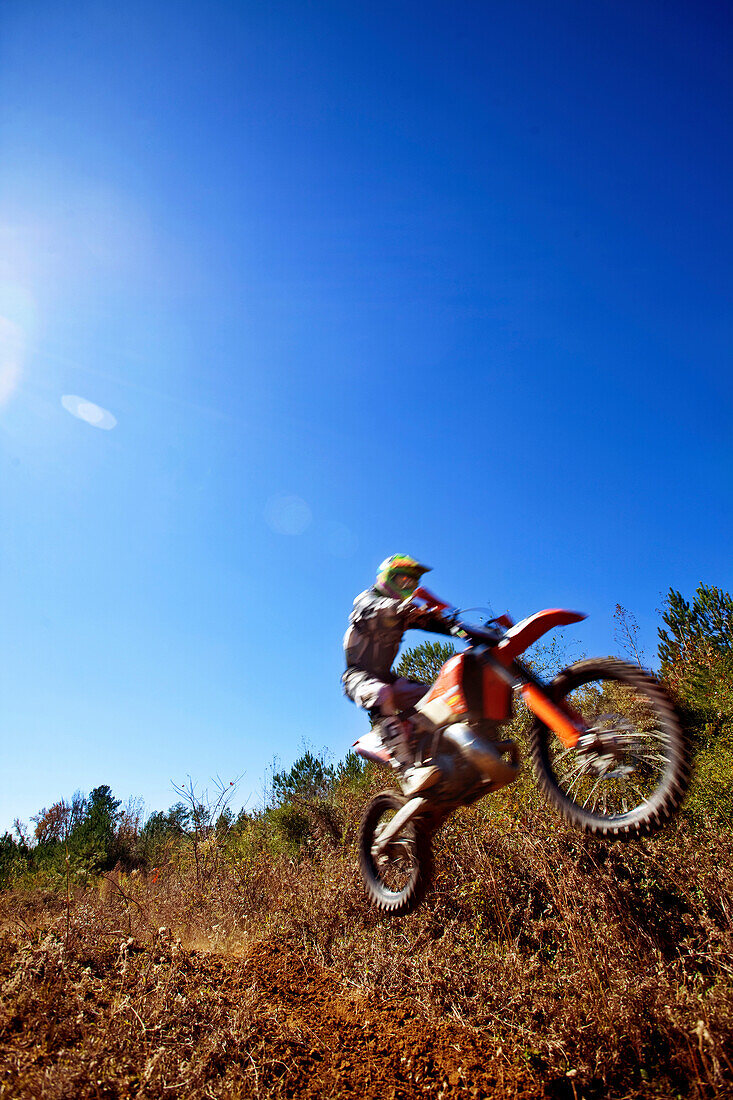 A motorcyclist catches air on a jump during an Enduro race in Maplesville, Alabama. (Back lit, Lens Flare, Motion Blur), Maplesville, Alabama, United States