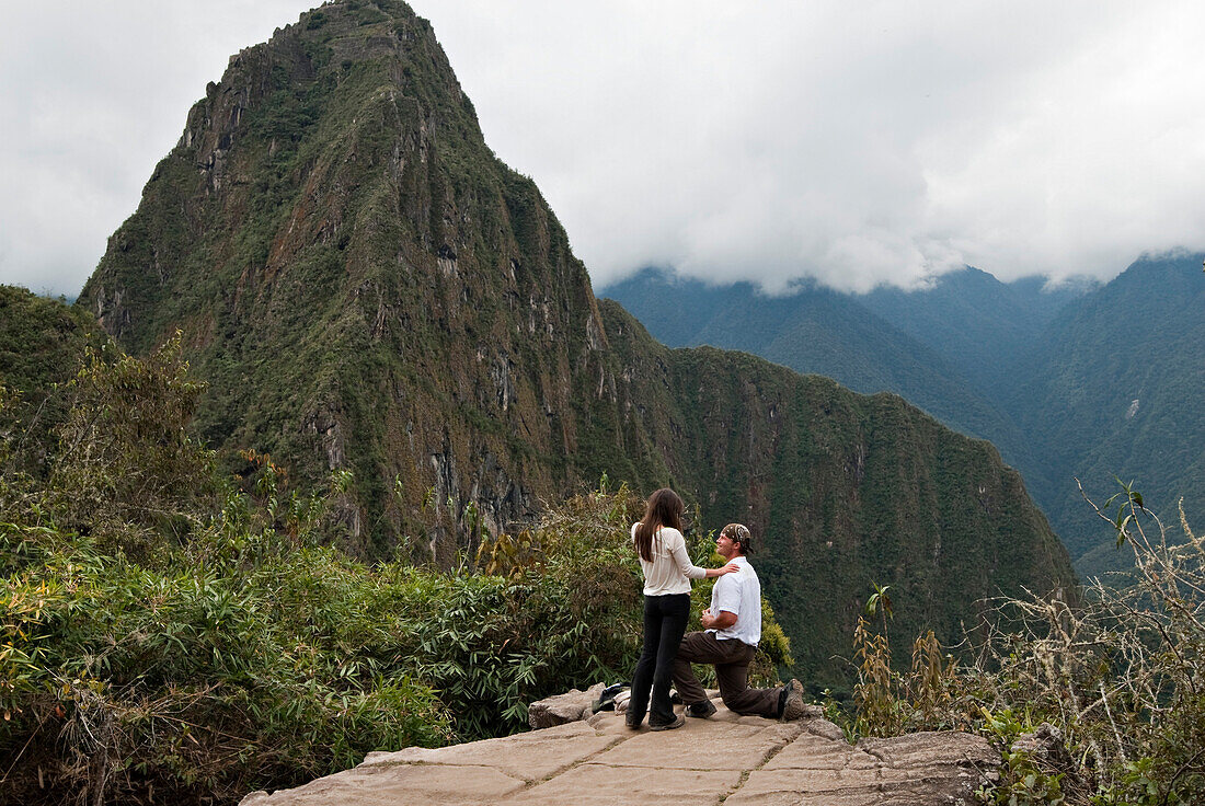 A young man asks for a young woman's hand in marriage in the ruins of Machu Picchu Inca Trail, Andes Mountains, Peru