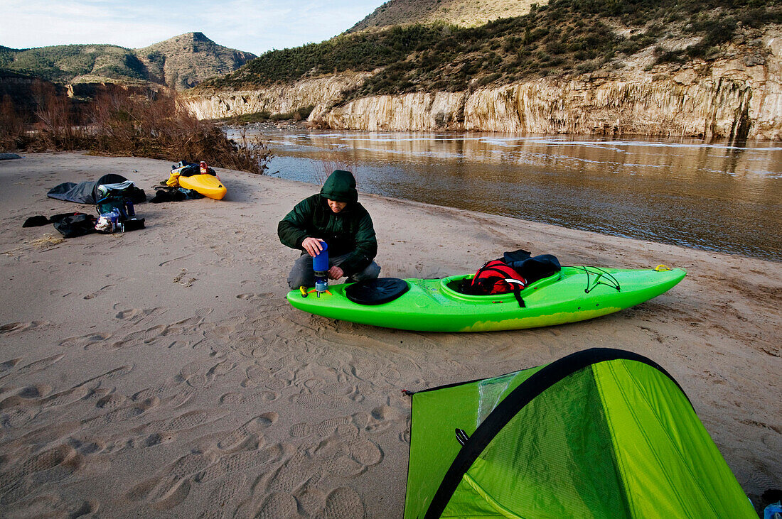 A middle age man heats water for coffee after a cold night camped along the Salt River, AZ AZ, USA