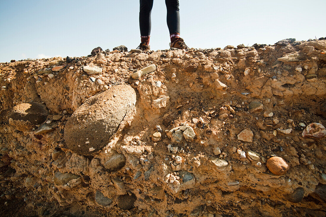 A girl stands on the edge of an eroding mesa bluff, with stones and soil exposed, in the badlands of Utah Utah, USA