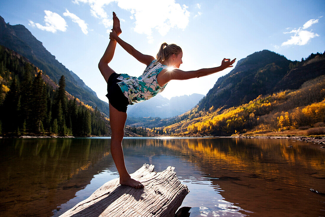 A young woman doing yoga next to a lake surrounded by glowing aspen trees Aspen, Colorado, USA