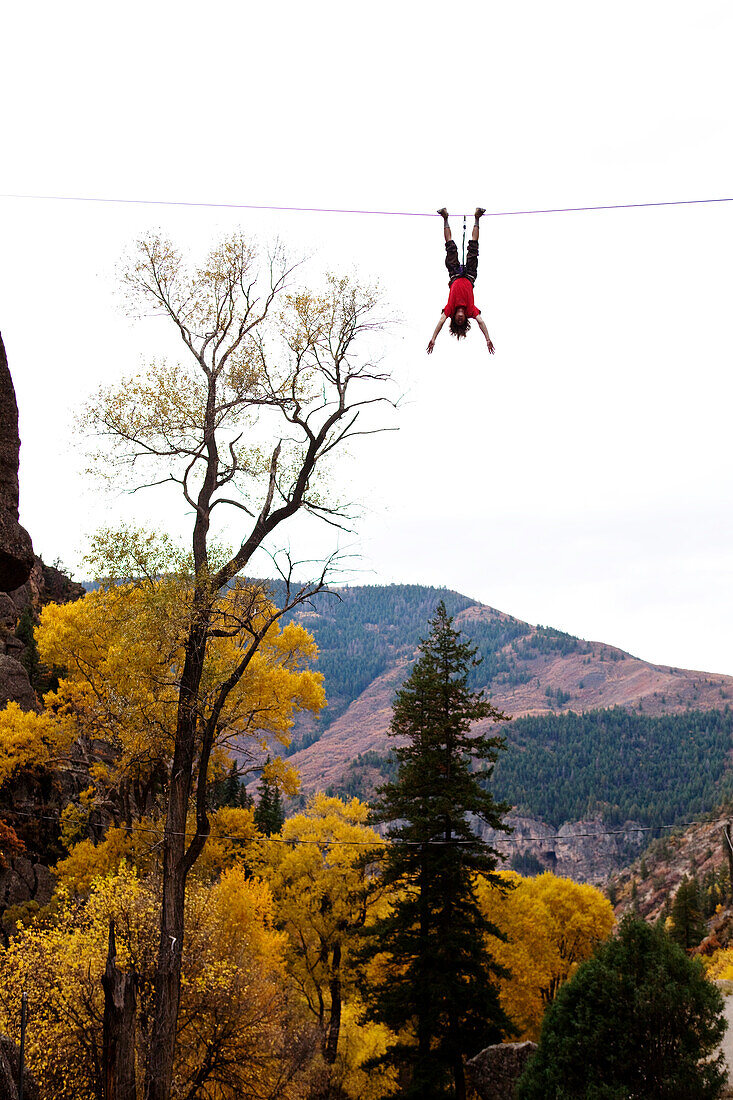 A young man does a bat hang from a slack line after walking the line Glenwood Springs, Colorado, USA