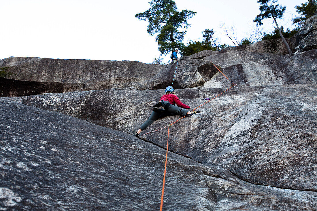 A female climber stems out while climbing pitch six of the Standard Route on White Horse in North Conway, New Hampshire Conway, New Hampshire, United States of America
