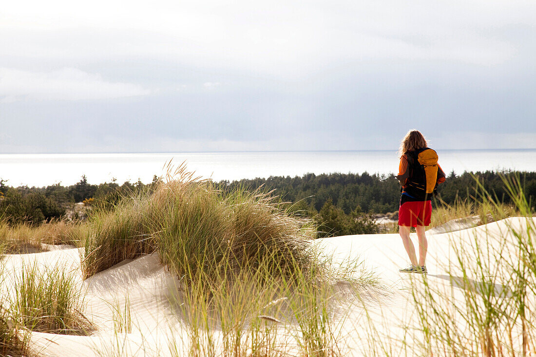 A girl walks alone on the sand dunes wearing a backpack Oregon, USA