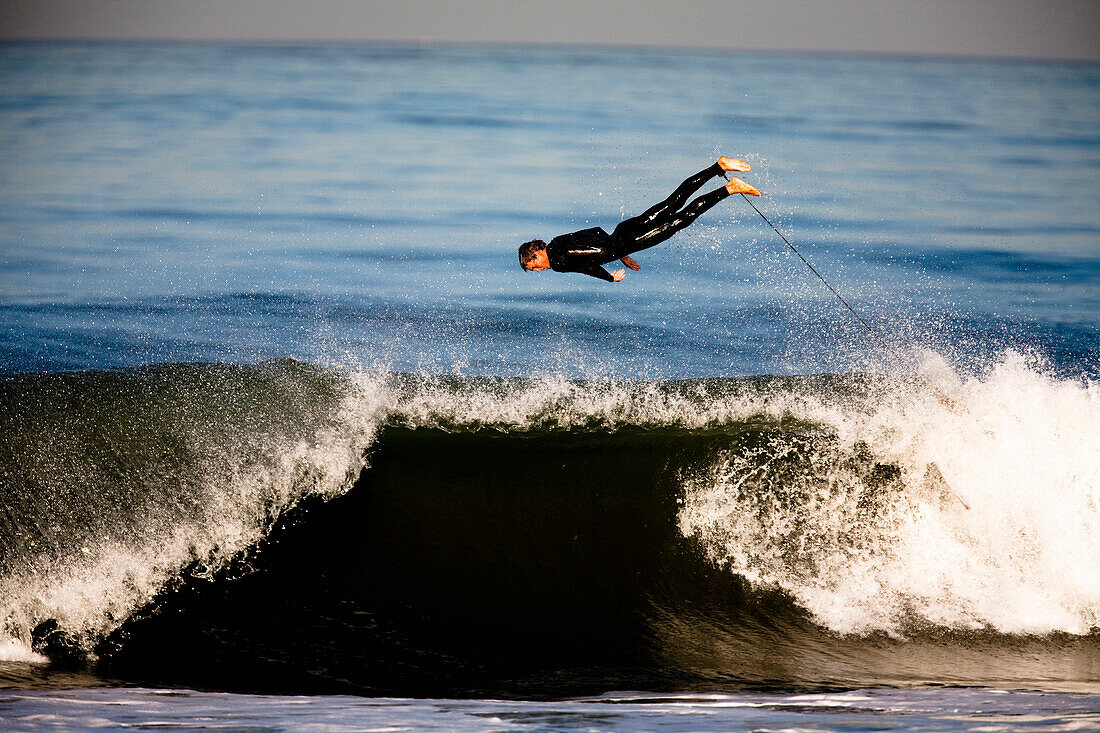 A male surfer jumps over the top of a breaking wave in Ventura, California Ventura, California, Unites States of America