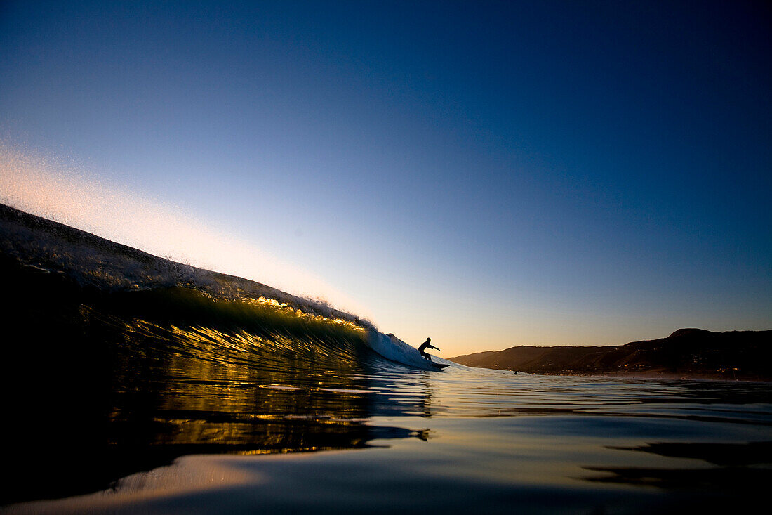 A male surfer does a bottom turn on a golden left while surfing at Zuma Beach in Malibu, California Malibu, California, Unites States of America