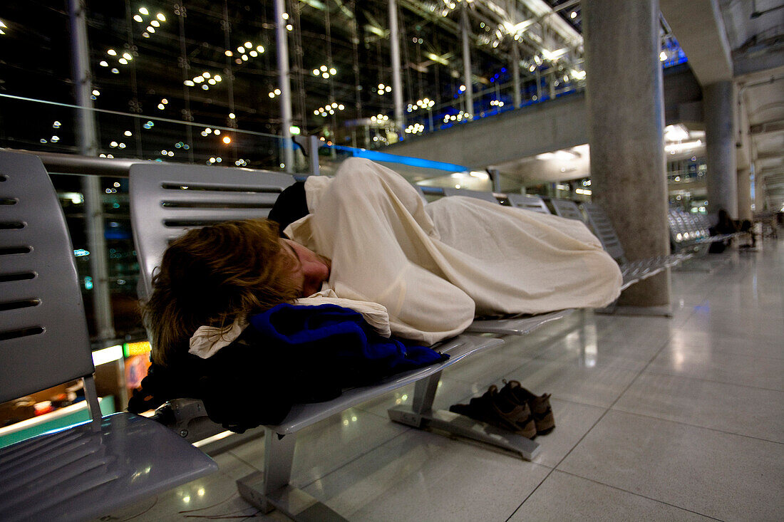 A male traveler sleeps on a bench in the Bangkok International Airport in Bangkok, Thailand Bangkok, Bangkok, Thailand