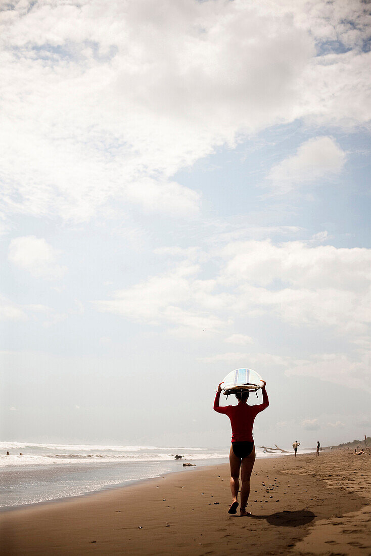 A woman walks down the beach with her surfboard resting on her head Dominical, Costa Rica