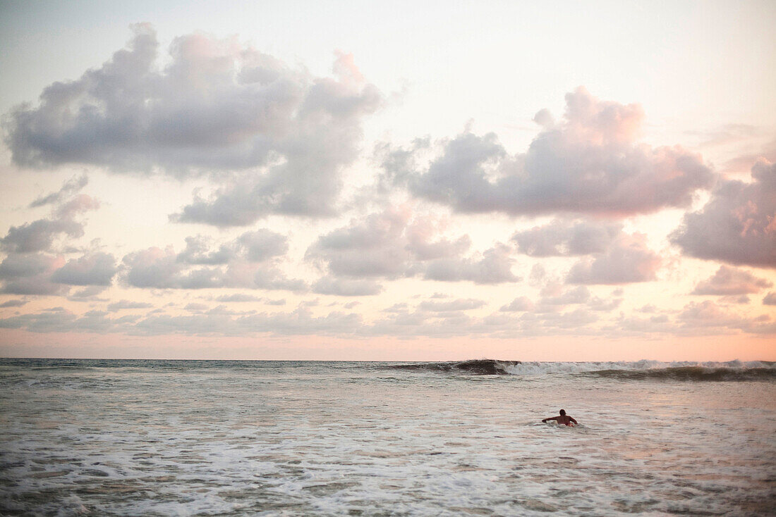 A man paddles out to catch the last waves of the day at a popular surfing spot Dominical, Costa Rica