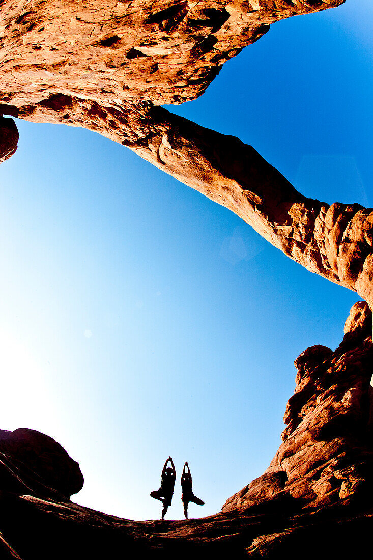 Couple doing tree posture yoga under the turret arch in Arches National Park Moab, Utah, USA