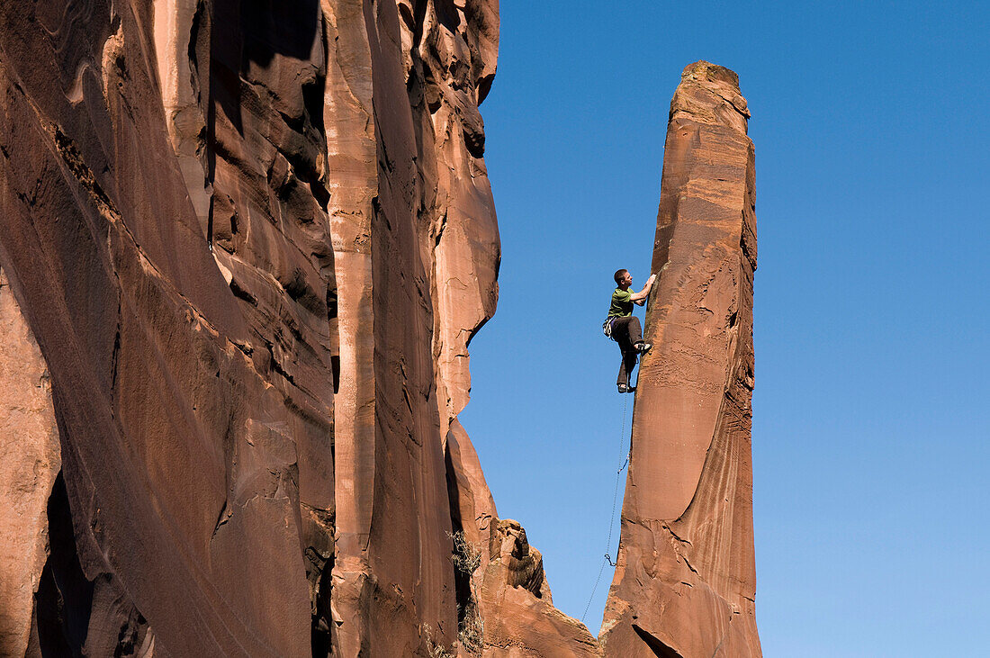 Man rock climbing up slender sandstone spire, Gateway, Colorado Gateway, Colorado, USA