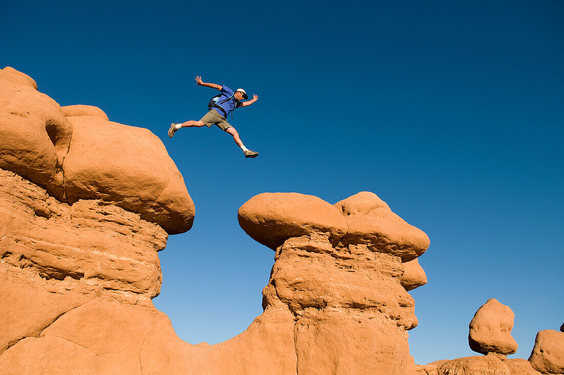 Man jumping between rock spires, Goblin Valley State Park, Hanksville, Utah Hanksville, Utah, USA