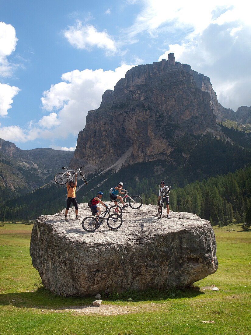 Four mountain bikers are standing with their bikes on a big boulder in a mountain meadow in the Italian Dolomites Val Gardena, Dolomites, Italy